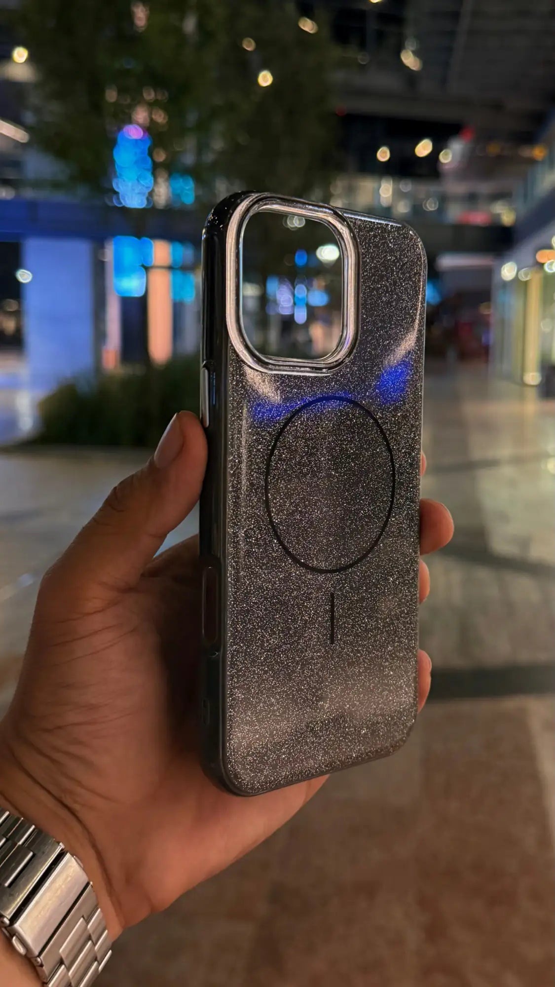 Funda de teléfono con brillo plateado y purpurina, con una almohadilla de carga magnética circular y recorte transparente para la cámara.