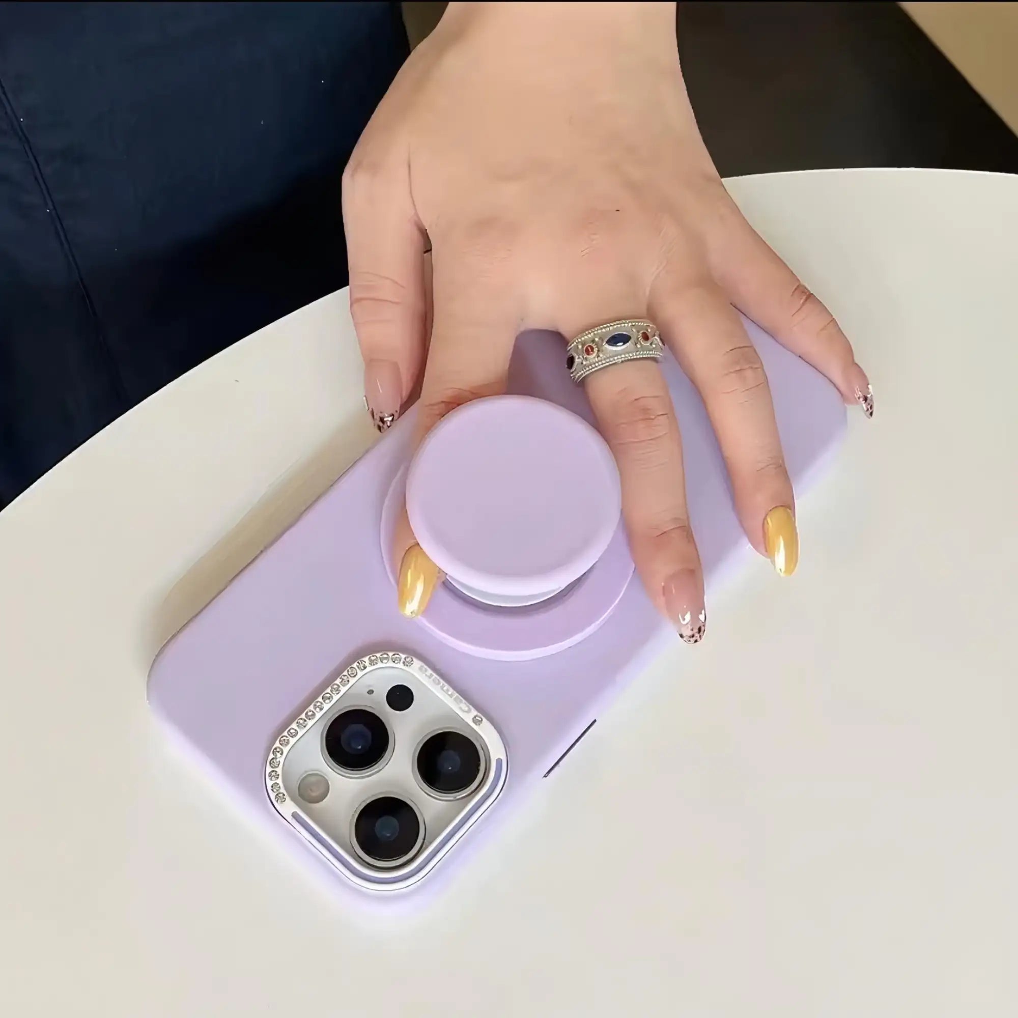 Funda de teléfono de color lila con una cubierta de lente de cámara incrustada con piedras preciosas plateadas.