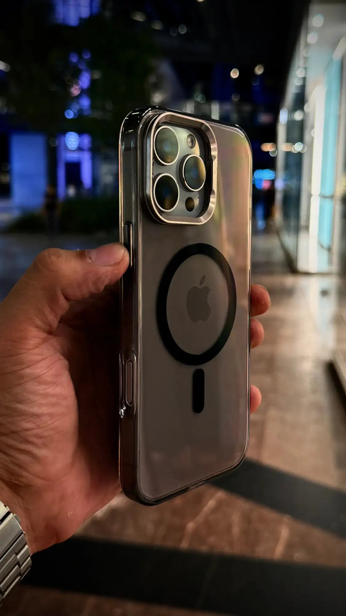 Una funda de teléfono elegante y transparente con un marco metálico plateado y un logotipo circular de MagSafe integrado en la parte posterior.