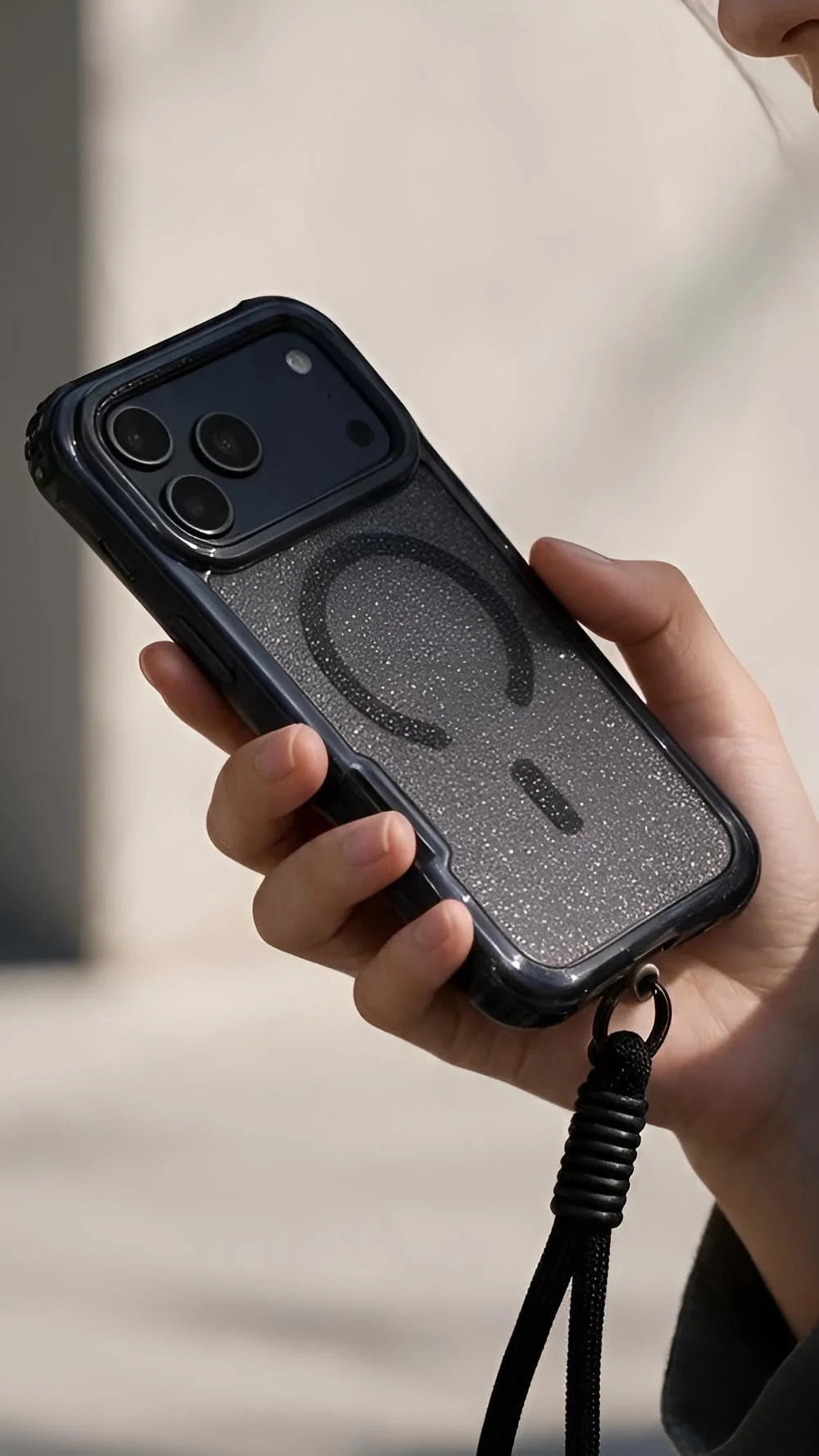 Vista trasera de funda negra súper glitter case magsafe con diseño de anillo magnético y correa trenzada negra