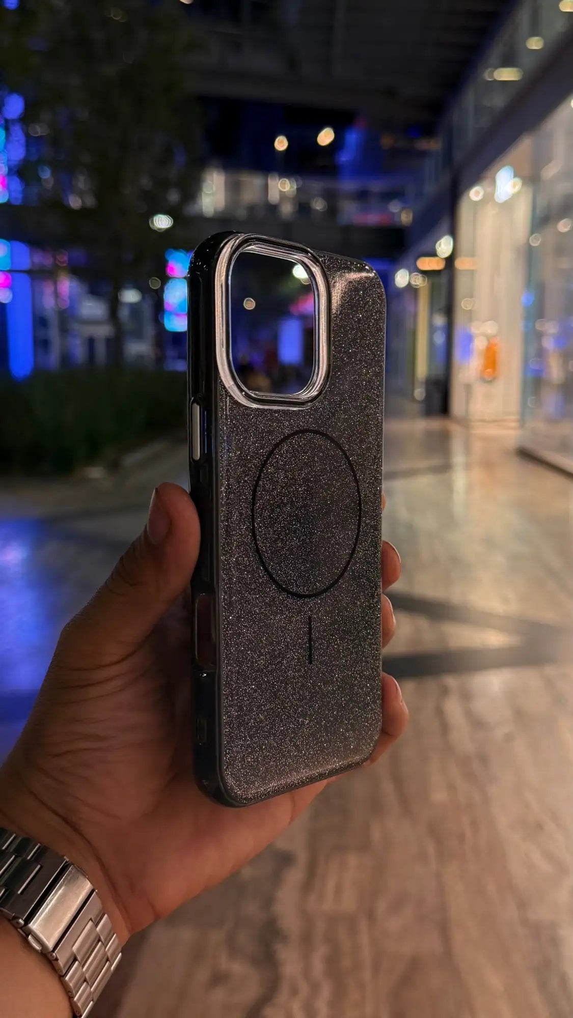 Funda de teléfono con purpurina negra, almohadilla de carga magnética circular y recorte para cámara plateado.