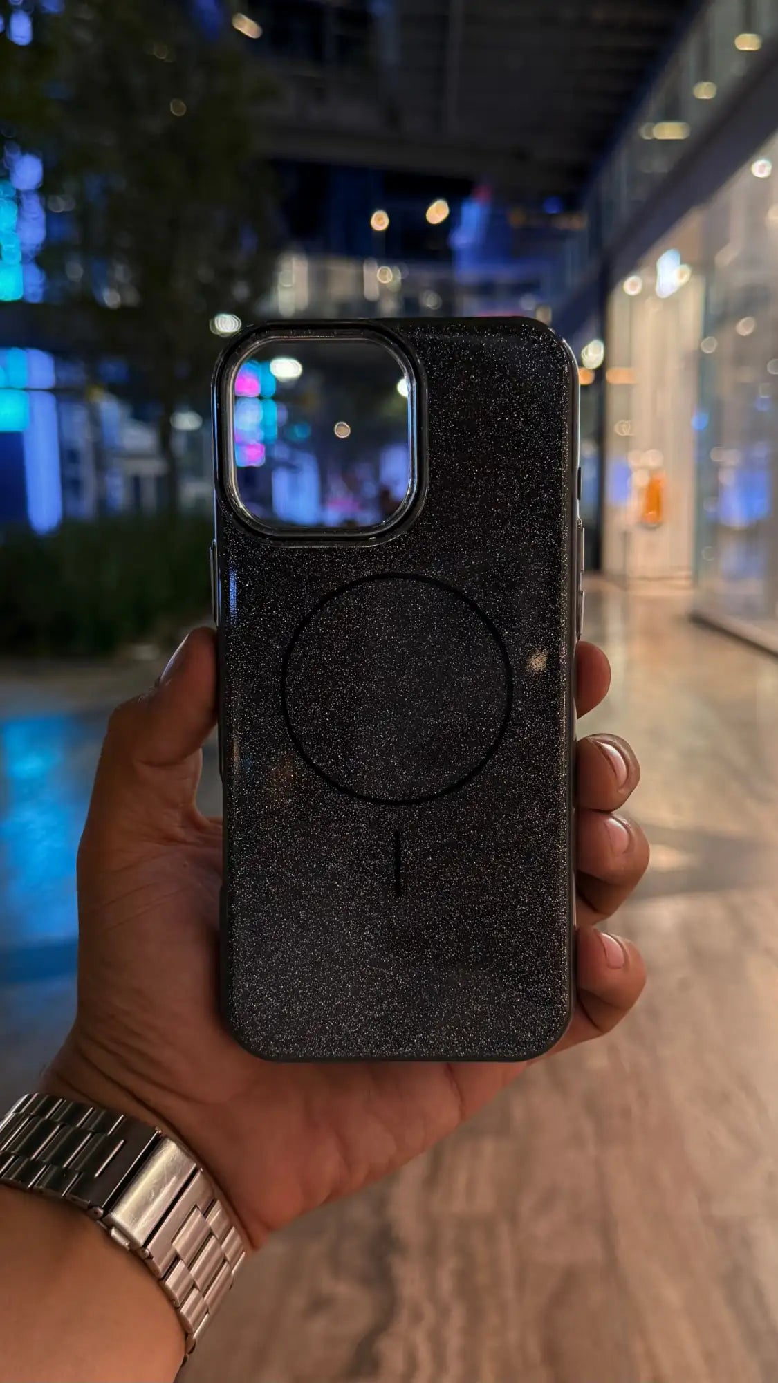 Funda de teléfono con purpurina negra y almohadilla de carga MagSafe circular.